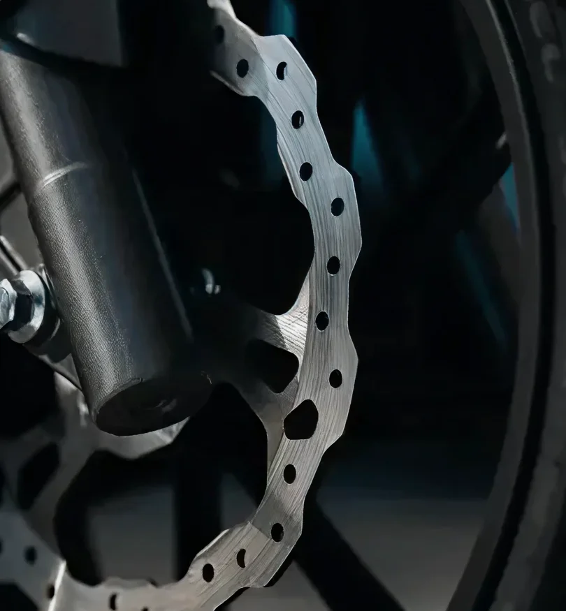 Close-up of a perforated metal disc brake rotor on a vehicle wheel.