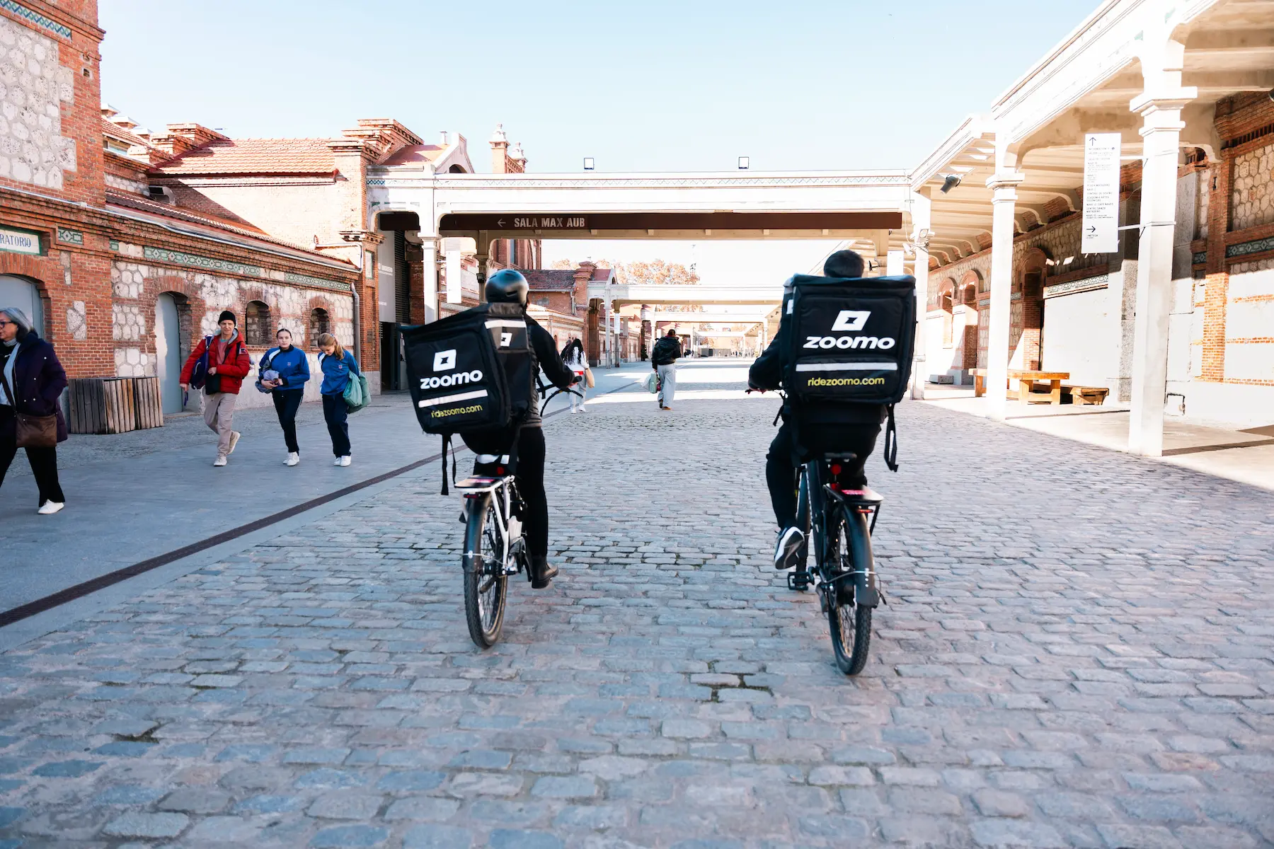 two delivery riders cycling around buildings with their bikes